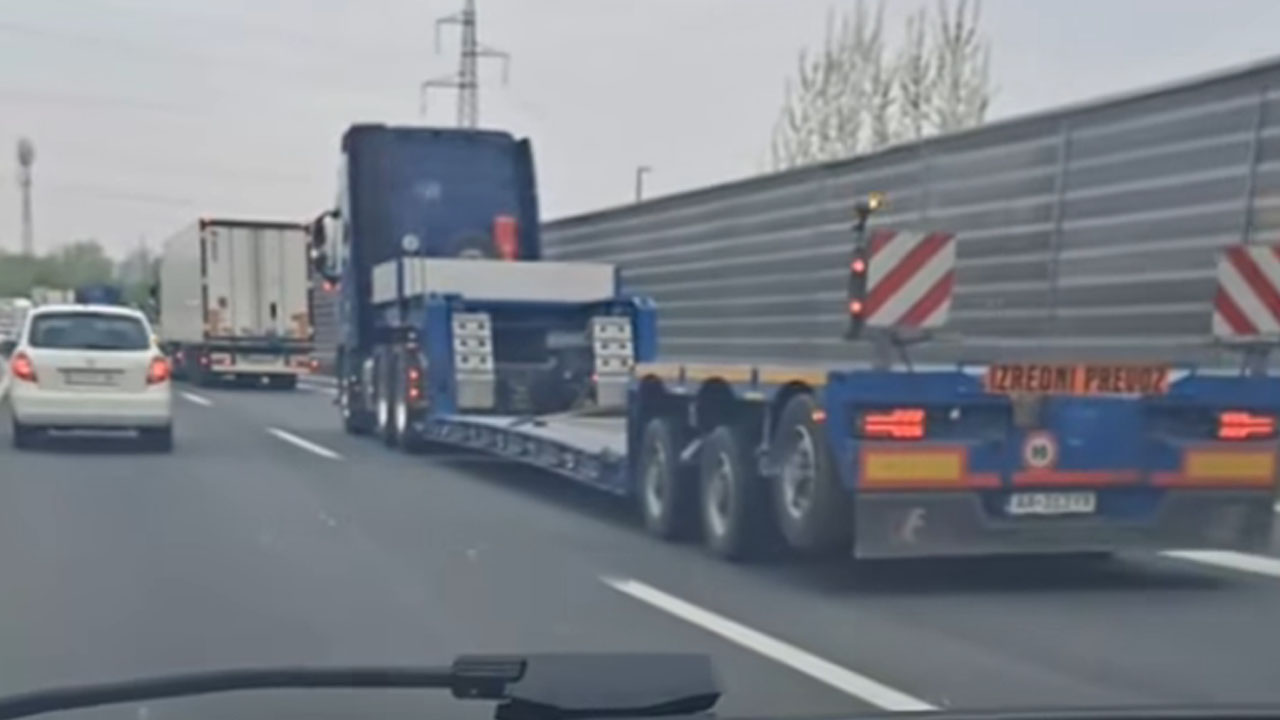 Tovornjak z ogromno prikolico, na kateri stoji majhen otroški avtomobilček