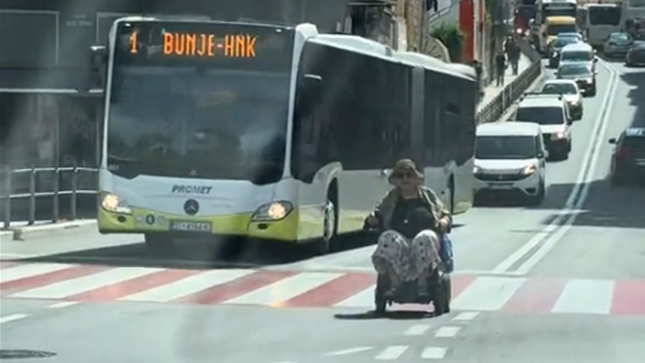 Starejša gospa na invalidskem vozičku vozi po sredini ceste v Splitu pred avtobusom